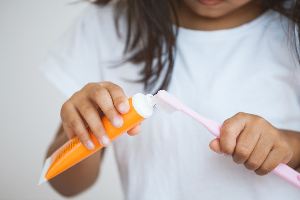 child putting toothpaste on toothbrush