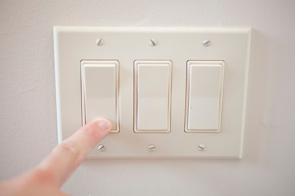 A finger switching off a light switch. Kids conservation tips